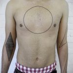 Black linework tattoo featuring a circle, diamond, and lines on the chest and arm, showcasing a minimalist and abstract design.