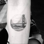 Black and grey realism tattoo of the Golden Gate Bridge within a circular frame on the forearm, showcasing a detailed and iconic landmark.