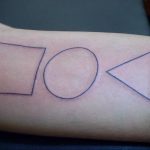 Black linework tattoo on the forearm featuring a square, circle, and triangle in a linear arrangement, representing basic geometric forms.