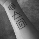Black line tattoo on the forearm featuring a circle, triangle, and maze symbol arranged vertically in a minimalist style.