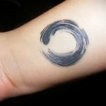 Watercolor-style Enso circle tattoo on wrist, black ink, minimalist, Zen Buddhist symbolism, flowing brushstroke effect.