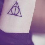 Black linework tattoo of the Deathly Hallows symbol on the inner forearm. A classic and recognizable tattoo design.