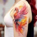 A vibrant watercolor phoenix tattoo on the upper arm, featuring flowing feathers, fiery colors, and a dynamic composition, showcasing rebirth and resilience.