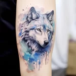 Watercolor style wolf tattoo on forearm, featuring realistic portraiture, blue and grey tones, and dynamic splash effects. A stunning ink idea.