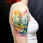 Watercolor tattoo of a forest scene with tall trees and a colorful sky on the shoulder. Features a blend of greens, blues, and yellows.
