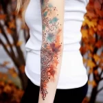A watercolor-style tattoo sleeve on a forearm, featuring abstract floral patterns and a blend of blue, orange, and brown tones with delicate linework.