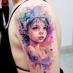 Watercolor-style tattoo of a young girl's face with vibrant splashes of color on the shoulder, showcasing realism and artistic flair.