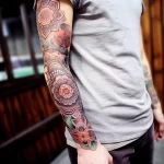 Detailed floral sleeve tattoo featuring ornate lotus blossoms and geometric patterns, covering the forearm and extending towards the elbow.