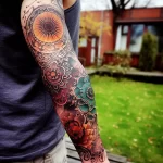 Full arm sleeve tattoo featuring a colorful mandala design with floral elements, incorporating shades of orange, teal, and red in a detailed style.