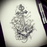 Black and grey tattoo sketch featuring an anchor adorned with flowers and a flowing ribbon, ideal for a sleeve or back piece.