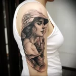 Black and grey realism tattoo of a woman in a hat, side profile, on the upper arm. Detailed shading and portrait style.
