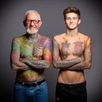A portrait of a father and son, both heavily tattooed with colorful, organic designs, showcasing a shared passion for tattoo art.