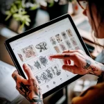 Close-up of hands interacting with a tablet displaying various tattoo sketches, featuring traditional and illustrative designs, showcasing digital tattoo art.