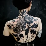 A large-scale blackwork floral tattoo covering the back, featuring detailed roses, leaves, and vines in a dramatic and elegant style.