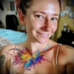 A watercolor-style butterfly tattoo on the upper chest and shoulder, featuring vibrant blues, yellows, and purples. The design is delicate and flowing.