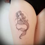 Black and grey fineline mermaid tattoo on the thigh, featuring flowing hair, a detailed tail, and a circular frame, creating a serene and elegant tattoo design.