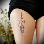 Black ink wildflower tattoo on the thigh, featuring a delicate arrangement of small flowers and dotted lines. A minimalist and natural tattoo design.