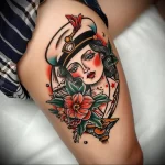 Traditional sailor tattoo with a woman in a cap, flowers, and a red star on the thigh. Vibrant colors and bold lines.