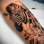 Black and grey realism zebra head tattoo with floral accents on the forearm, showcasing intricate details and soft shading. A beautiful animal and floral tattoo.