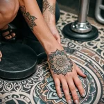 Detailed black and grey mandala tattoo on a woman's hand, featuring intricate geometric patterns and floral elements. A beautiful and symbolic design that adorns the back of the hand.