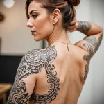 Large black and grey tattoo on a woman's back and shoulder, featuring intricate Celtic knotwork and flowing patterns. A detailed and elegant design that follows the body's curves.
