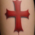 Bold red ink tattoo of a classic cross shape with a dripping effect, simple yet striking design, calf placement.