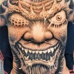 Extremely detailed black and grey tattoo covering the face, depicting a monstrous creature with sharp teeth and horns. A bold and intense tattoo art piece.